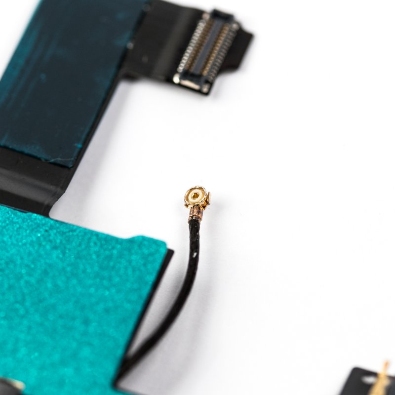 Macro view of the flex cable's teal tape with the gold coaxial antenna connector and its thin black cable curving away, on white.