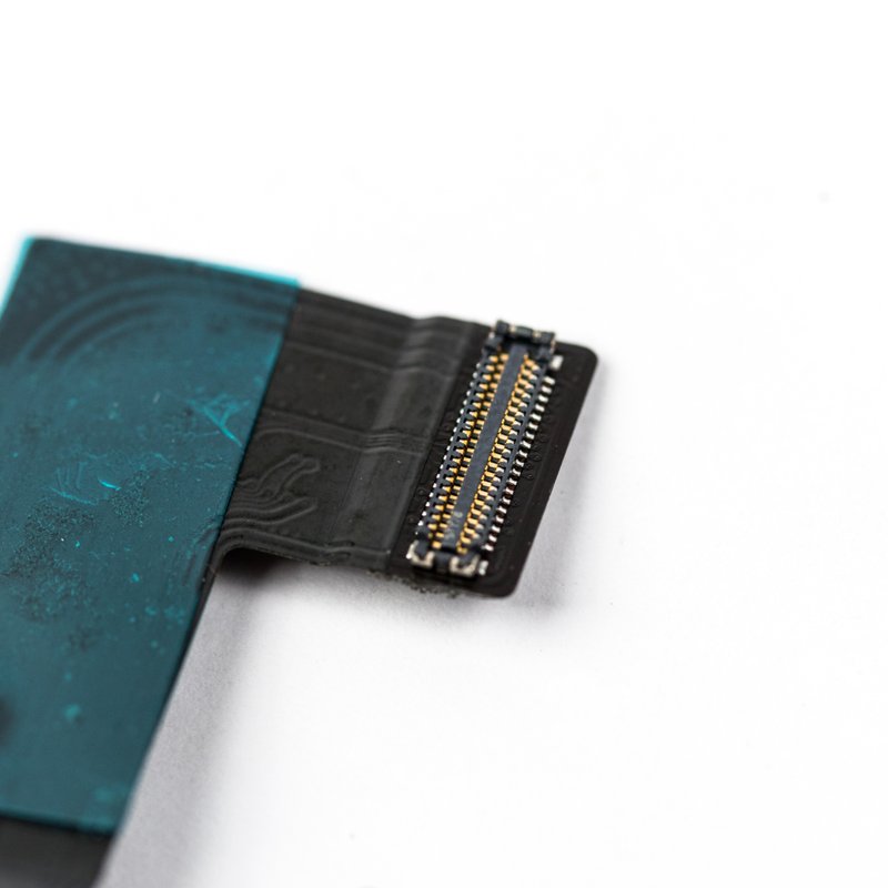 Macro view of the flex cable's gold-pinned board-to-board connector beside its teal antenna tape, photographed against a plain white background.
