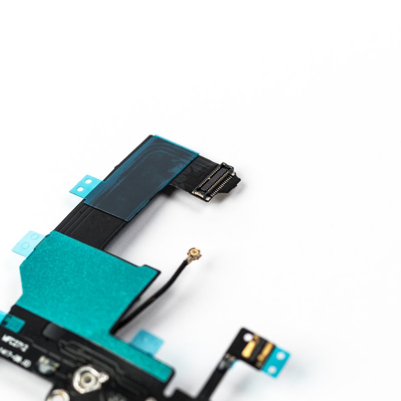 Macro of the white iPhone 5 charger flex, focused on the gold pin logic board ribbon connector with the coaxial antenna plug and green shielding tape below.