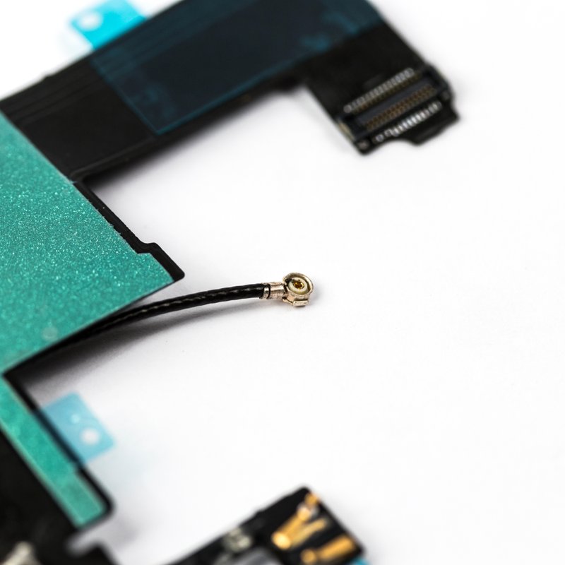 Macro detail of the black iPhone 5 charger flex showing the green shielding tape, the gold coaxial antenna connector on its short black lead and teal protective tabs.