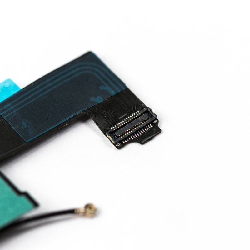 Macro of the black iPhone 5 charger flex end, showing the gold pin logic board ribbon connector, dark blue backing film and the out of focus coaxial antenna plug.