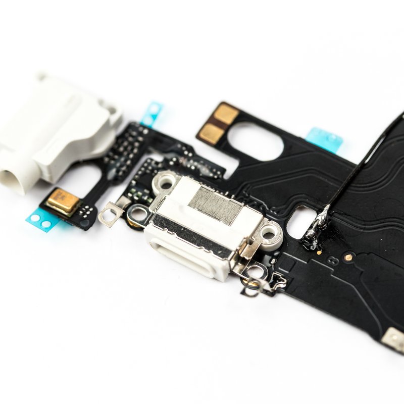 Angled close-up of the iPhone 6 charging port flex, with the white headphone jack and white Lightning connector in focus and the black flex running away behind.
