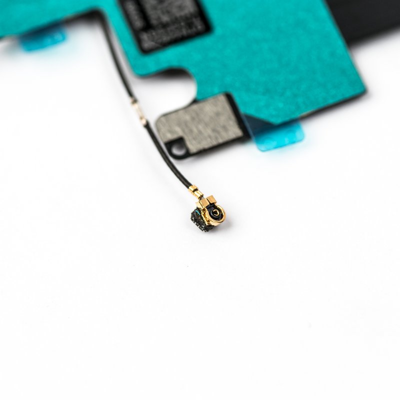 Macro view of the gold coaxial antenna connector on the iPhone 6 charging flex, with the teal EMI shield and a blue protective tab filling the frame.