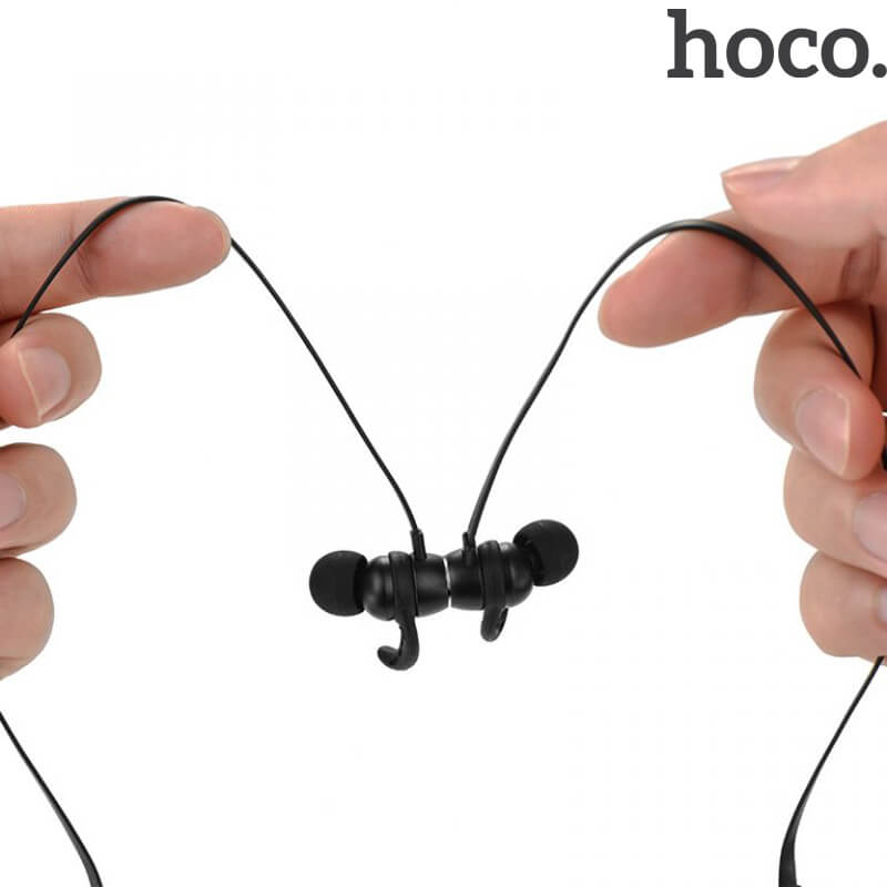 Hands holding the black HOCO ES11 Maret Bluetooth earphones by their flat cables with the magnetic earbuds joined together in the middle, hoco logo top right.